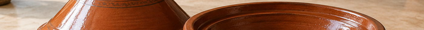 Terracotta tajine met schaal en deksel naast een kommetje olie, klaar voor het eerste gebruik